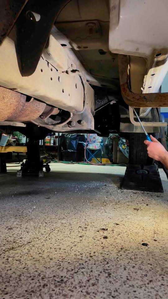 Coating being sprayed along the underside of a vehicle with a wand